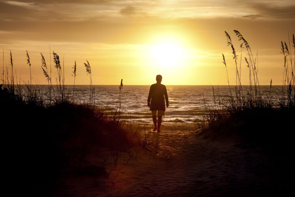 A person walking alone toward the sunrise, symbolizing resilience and hope.